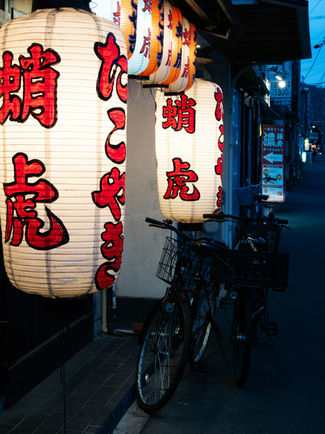 Collage gastronómico de Japón: un bowl de ramen caliente en una mesa de madera, la fachada iluminada de restaurantes callejeros, una fila de clientes comiendo en cabinas individuales estilo Ichiran, y faroles japoneses tradicionales colgando en una calle nocturna.