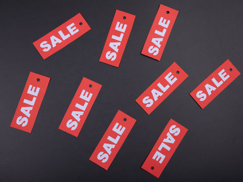 Red "SALE" tags scattered on a dark surface. Bright white text contrasts with the bold red, creating a vibrant promotional display.