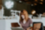 woman with red hair sitting at a table and working on her laptop