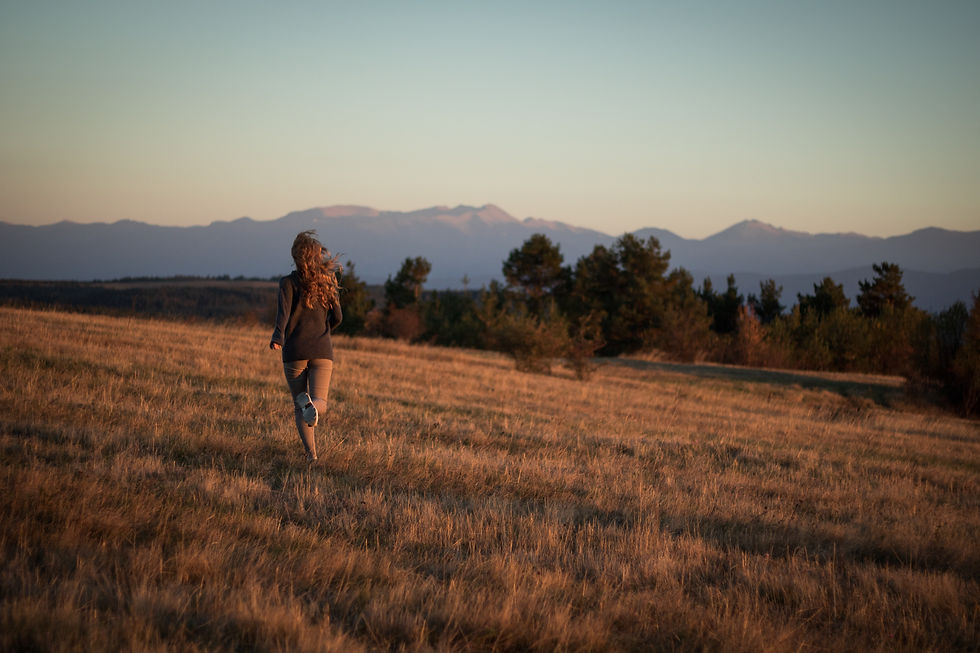 Woman running across a field with trees and mountains in the background