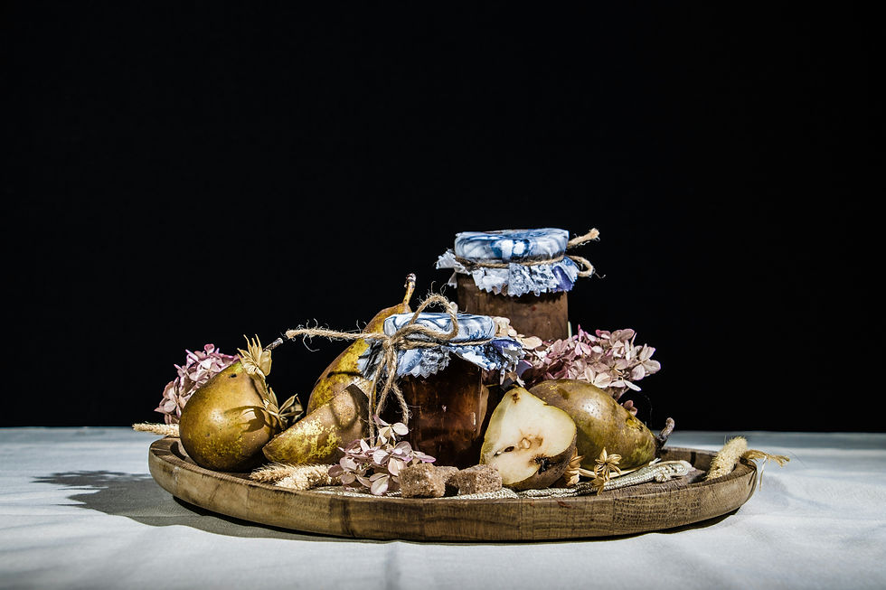 A rustic arrangement showcasing jars of homemade caramelized pear jam with vanilla bean, surrounded by fresh pears and decorative dried flowers on a wooden platter.