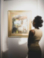 From behind view of a Black woman looking at a framed piece of abstract art hanging up on a wall.