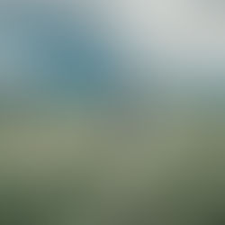 Person with a blue backpack takes a photo of a stormy landscape. Green fields and mountains under dark clouds create a dramatic scene.