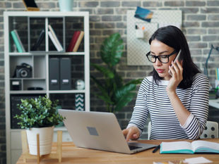 A woman working on a laptop while on the phone