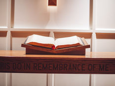 Open Bible on a church pulpit carved with the words “Do This in Remembrance of Me,” symbolizing reflection on church leadership and faith.
