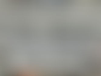 Aerial view of a concrete building under construction, covered with protective white netting. The rooftop and surrounding cityscape are visible.