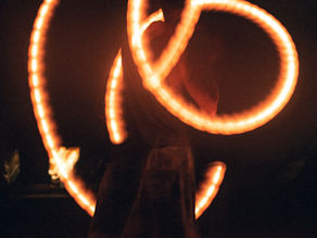 A performer spins glowing fire poi in intricate patterns against a dark background, creating bright, swirling light trails.