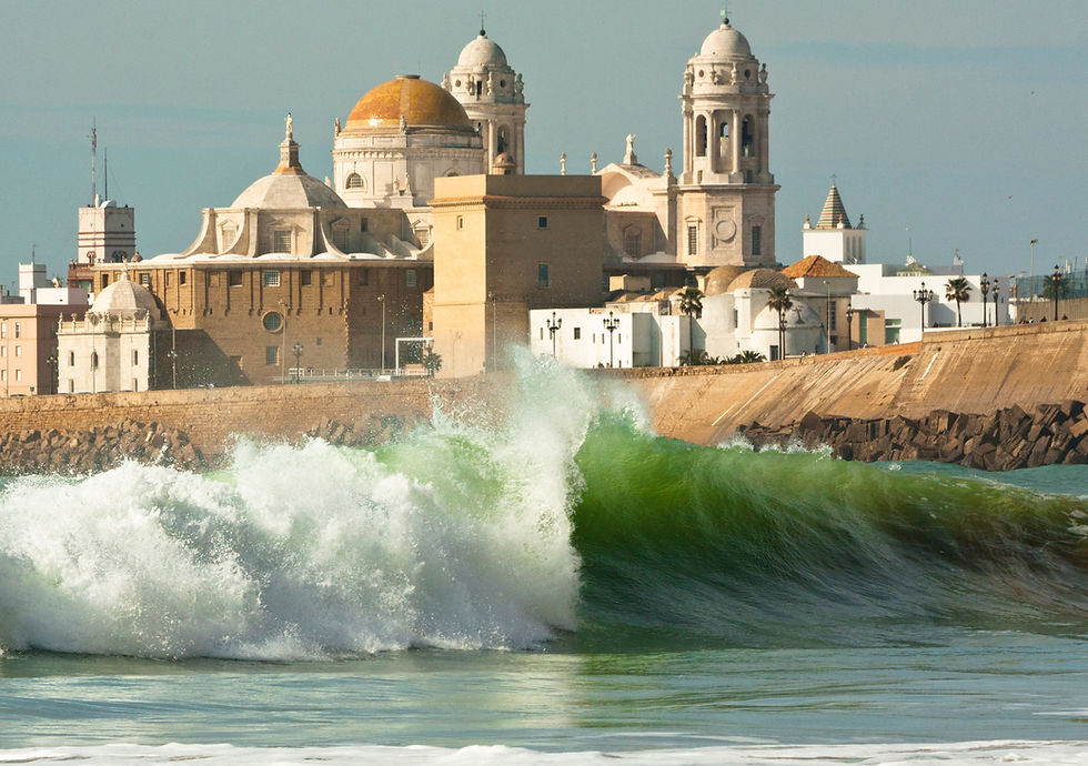 Majestic ocean waves crash against the shore, with the stunning Cádiz Cathedral standing prominently in the background, showcasing the blend of natural beauty and historic architecture in Cádiz, Spain.