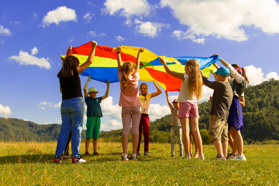Children holding a colorful parachute up in a field on a sunny day.