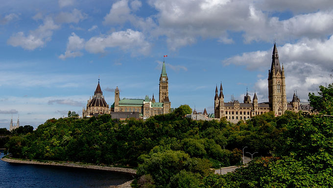 Parliament Hill above the Ottawa River, surrounded by green trees.