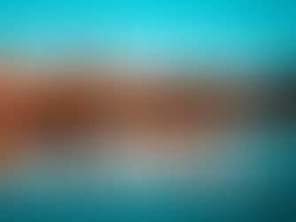 Beautiful evening view of Muscat's waterfront with mosque minaret, illuminated buildings, and calm reflections on the water under a vibrant blue sky.