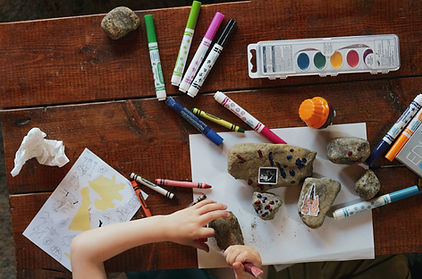 A child's hand, using drawing pencils and crayons for learning purposes.