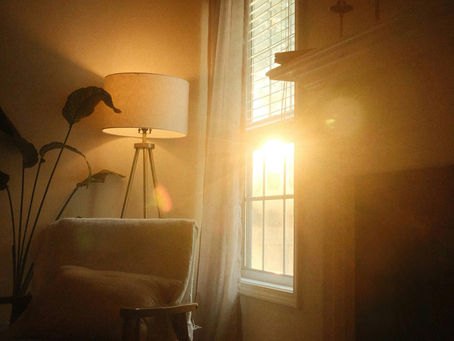 Sunlight streaming through a window beside a cozy chair and lamp, creating a warm, peaceful Casita sanctuary atmosphere.
