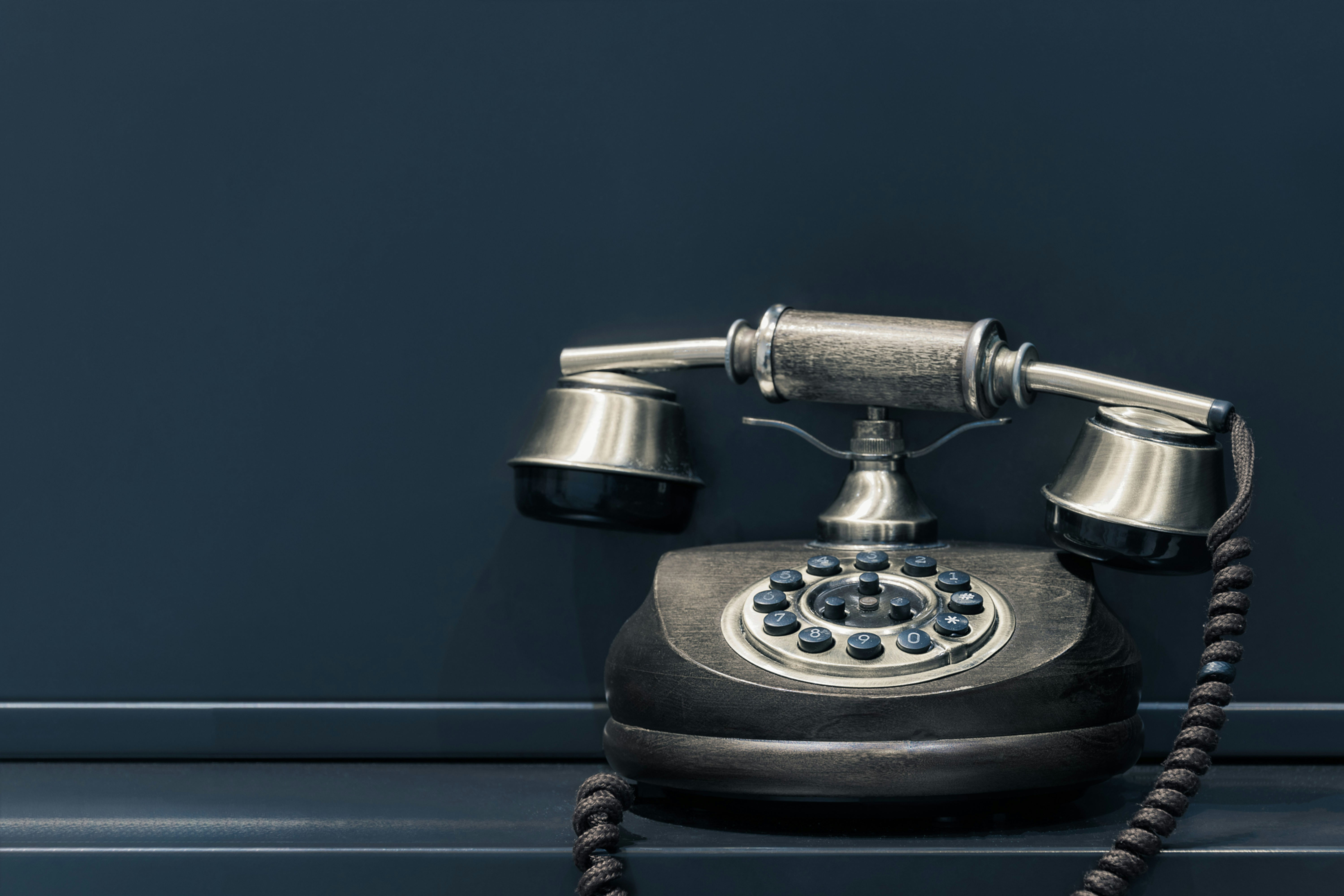 A stylish vintage, dark metallic rotary phone set offcenter against a dark background.