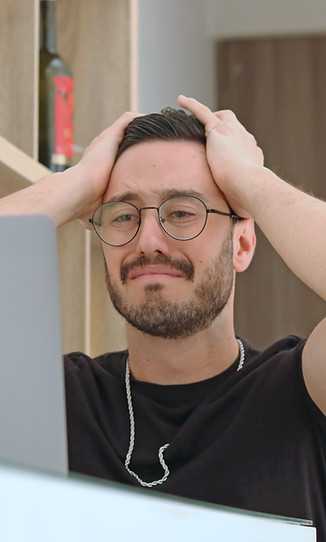 A frustrated graphic designer stares at his laptop with both hands on top of his head.