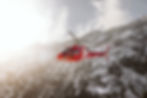A red helicopter soars through the snowy mountain range.