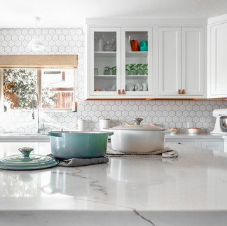 Un espace cuisine équipée et moderne, avec des armoires blanches, un plan de travail en marbre blanc et élégant où sont disposés des casseroles.