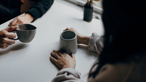 Two people share a quiet moment over coffee, their hands cradling warm mugs at a sunlit table.
