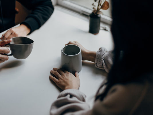 Image of two people meeting together for conversation and coffee, image cropped to just hands and coffee mugs
