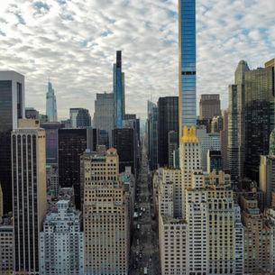 Aerial view of Midtown Manhattan with high-rise buildings and city streets beneath a dramatic sky.
