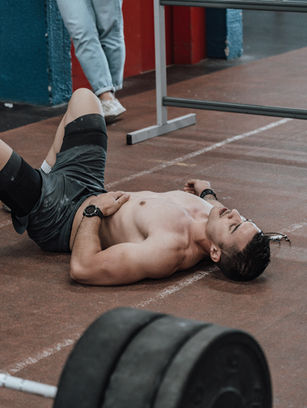 Man lying on gym floor near weights, tired and showing signs of B12 deficiency.
