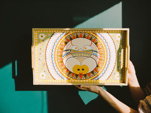 Hand holding a painted wooden tray with a colorful, symbolic Tunisian design, lit by natural sunlight — representing intention and beauty in gifting