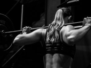 A girl with a barbell on her back in workout clothes.