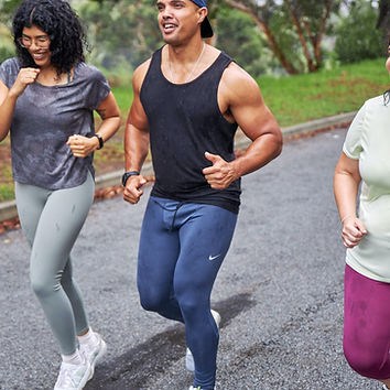Three diverse people running outdoors, smiling along a path, active lifestyle, fitness goals.