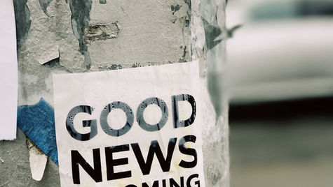 A white poster on a lamppost that states 'GOOD NEWS IS COMING'