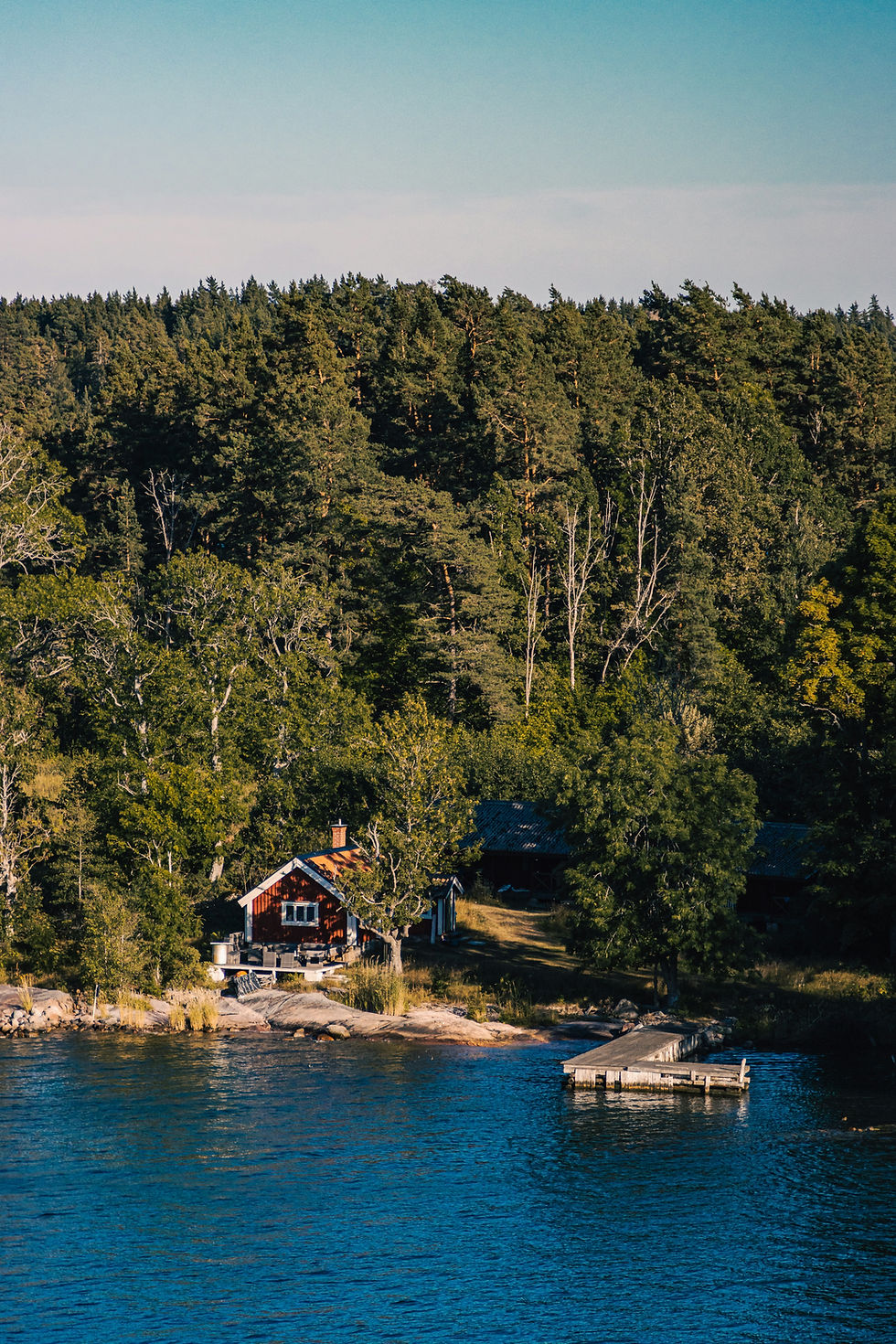 Cabane rouge au bord d’un lac bleu, ponton en bois et forêt dense en arrière-plan, ambiance paisible.