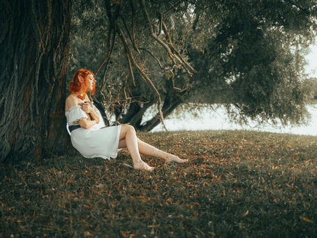 Woman resting against a large tree by the water, representing allowing yourself to receive support from the Earth.