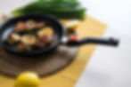Pan with roasted chicken, garlic, and lemon slices on a woven mat. Green onions and a yellow napkin are visible in the background.