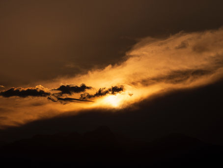 Sunset over mountains with dramatic clouds and orange hues in the sky, creating a peaceful and mesmerizing atmosphere. No text visible.