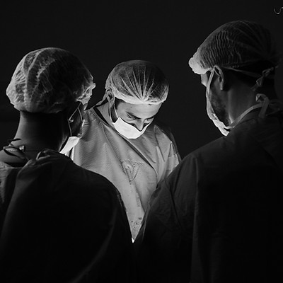Black-and-white photo of a specialized medical team in surgical scrubs, gowns, and masks gathered under surgical lighting for post-autopsy care.