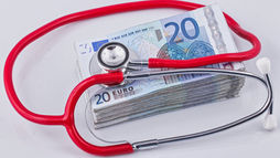 Stethoscope on a stack of 20 Euro bills, highlighting healthcare costs. Red tubing, white earpieces, and visible currency text.