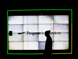 Silhouetted figure standing before a large illuminated wall display with the words “Progress is never done,” suggesting ongoing change and the unfinished future of work.