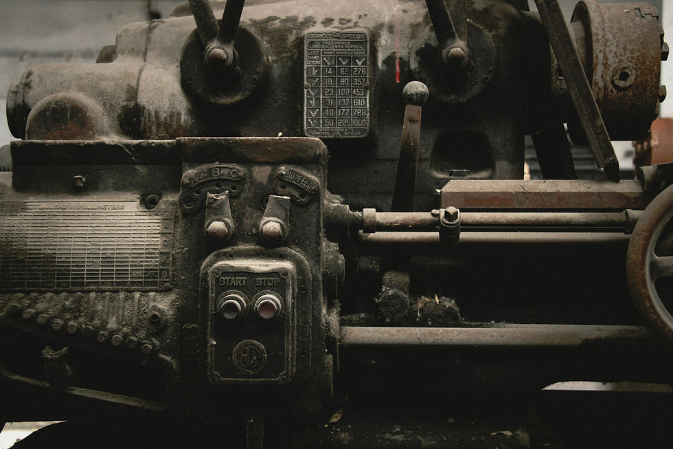 Close-up of a vintage industrial machine with rusty levers and dials. Buttons labeled "Start" and "Stop" are visible. Industrial setting.