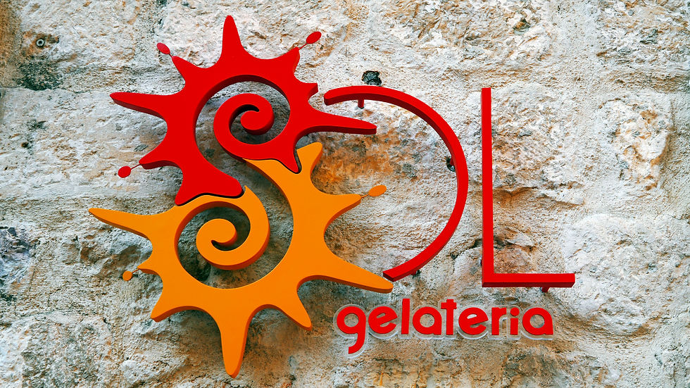 Red and orange sun-shaped logo for Sol Gelateria mounted on a stone wall, representing how color, typography, and design elements create a cohesive brand identity that fits a business’s personality.