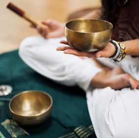 Person holding a singing bowl, meditating. Other bowls, accessories, and floor setting