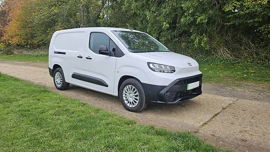 White compact commercial panel van parked on a rural gravel driveway bordered by lush green foliage