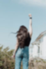 A woman with long hair wearing blue jeans and a black tank holding her hand in the air in celebration with clear blue skies.