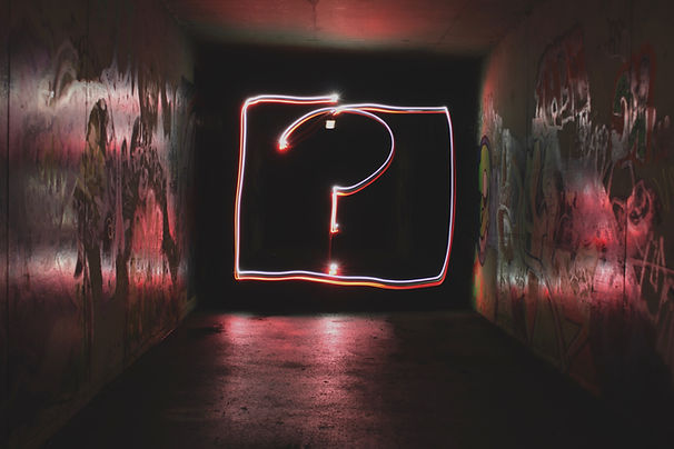 A neon lit question mark surrounded by a wall of graffiti