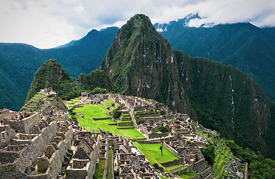 A high-angle view of the ancient Inca citadel of Machu Picchu in Peru, showcasing its terraced stone ruins and vibrant green plazas set against the backdrop of the iconic Huayna Picchu mountain peak under an overcast sky. Image by Eddie Kiszka