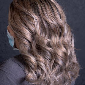 Eine Frau zeigt ihren Hinterkopf samt lockig geföhnter Balayage Haare