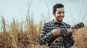 A smiling man playing a ukulele