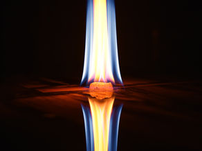 Orange and blue flame on a dark background, reflecting on a shiny surface. The atmosphere is calm and mesmerizing.
