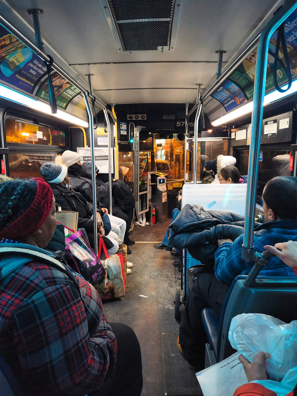 Passengers in winter clothing sit inside a bus at night, holding bags. The interior is lit by overhead lights, creating a cozy atmosphere.