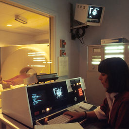 A patient undergoing an MRI as a provider manages controls behind the scenes.