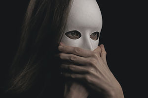 Person wearing a white mask covers mouth with hands, long hair visible. Dark background, mysterious and tense mood.