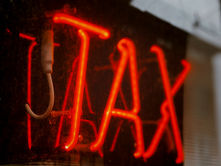 Red neon sign reading "TAX" glows against a dark reflective window, with abstract outdoor reflections and a moody ambiance.